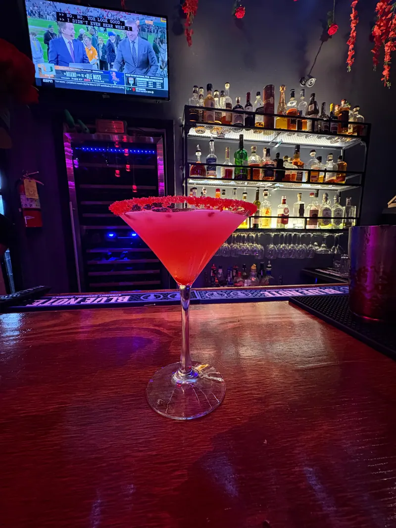 A red cocktail in front of the illuminated bottle shelves